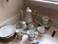 Full view of tea and coffee set including cups, saucers, plates, coffee pot, sugar bowl, creamer, and serving tray arranged on a countertop.