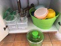 Photo of shelves with assorted plastic storage containers, including rectangular containers and a green basket holding several round containers in different colors.