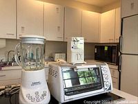 Full view of the three appliances placed on a kitchen counter: black toaster oven, white blender/food processor, and white can opener.