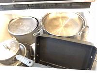 Photo showing multiple metal pots and pans including stockpots and a rectangular baker