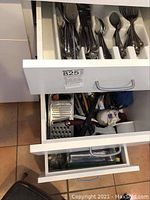Open kitchen drawers showing stainless flatware arranged in drawer organizer and kitchen utensils like graters and spatulas in adjacent drawers