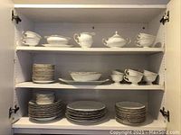 Full shelf view showing the stacked dinner plates and bowls, creamers, sugar bowls, and covered serving dishes all with white porcelain and gold trim