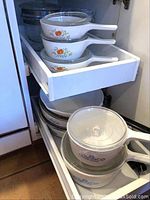 Three orange floral CorningWare handled saucepans and one Cornflower Blue saucepan with lid in a cabinet drawer
