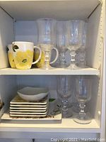 Shelf with 5 ceramic coffee cups with yellow floral pattern and 5 crystal goblet-style wine glasses