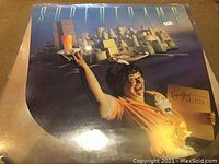 Front cover of Supertramp Breakfast in America LP featuring waitress holding breakfast items with cityscape of breakfast foods in background.