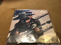 Front cover of the Stevie Ray Vaughan LP record featuring the artist playing guitar, protected in a plastic sleeve.