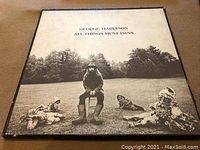Front cover of George Harrison 'All Things Must Pass' LP album showing George Harrison seated outdoors with three garden gnomes around him, brown tone.