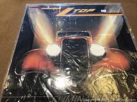 Front cover of ZZ Top vinyl LP showing red classic car with lit headlights under protective cover