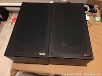 Front view of two vintage Audio Research AR 1AX speakers with black fabric grills installed on a table, showing slight dust and wear.