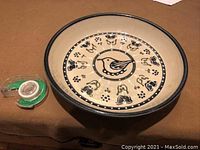 Top view of circular large ceramic bowl showing central bird motif with surrounding floral patterns, black rim, and cream background.