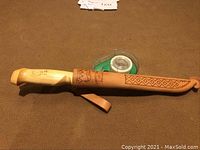 Knife in sheath on carpet with tape dispenser in background to indicate size