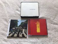 Lot of three Beatles CDs on white surface including sealed Abbey Road, White Album, and 1 CDs