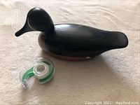 Black and teal painted wooden duck decoy with tape dispenser for scale, viewed from side angle.