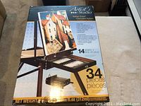 Box of Artist's Studio Italian Easel and 34-piece paint set showing artwork on easel and included items.