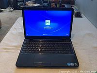 Front view of the Dell Inspiron laptop powered on to the Windows 7 login screen, showing the keyboard and screen.