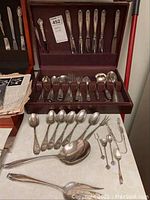 Velvet-lined wooden chest open to show knives in lid and forks, spoons, servers in tray