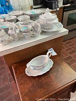 Set of porcelain china and serveware on a counter including cups, saucers, creamer, sugar bowl, platter and gravy bowl