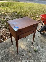 Full view of the vintage wooden side table with two drawers, showing scratches and surface wear on the top and the turned legs.