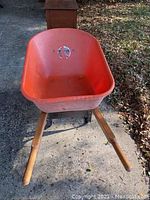 Front view of the orange plastic wheelbarrow showing basin and wooden handles