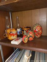 Photo of wooden shelf holding the painted eggs, ceramic cups with floral designs, and two vintage Pepsi bottles.