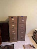 Two beige metal file cabinets standing side by side showing entire cabinets and context with nearby furniture.