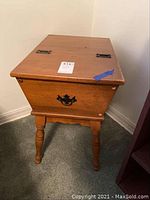 Full view of the vintage wooden sewing box with legs standing on carpeted floor against a wall.