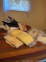 Various vintage blankets and covers of different materials and sizes placed on a bed and floor, some in plastic bags.