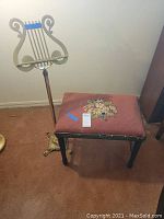 Front view showing the cherry bench with needlepoint floral cover and the brass lyre-shaped music stand.