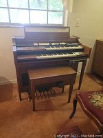 Photo showing full front view of the Baldwin electric organ with two keyboard manuals, pedalboard, and matching bench. Instrument positioned near window.