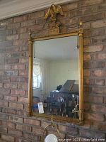 Gold-tone ornate mirror with eagle finial against brick wall
