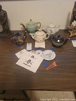 Group shot showing five teapots arranged on a wood surface with cards and drink stirrers nearby
