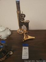 Front angle view of brass microscope showing full assembly on tripod base.