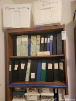 Overall view of wooden shelving unit showing two white styrofoam boxes on top shelf, row of binders on middle shelves, and plastic containers on bottom shelf