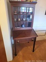 Full view of vintage secretary desk with glass display case showing slant top desk and contents inside glass panes.