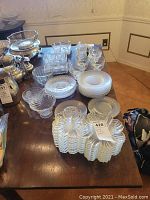 Wide view of assorted clear glass cups, plates, bowls, and serving dishes arranged on dining table.