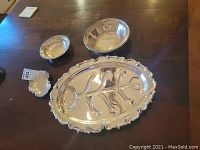 Top-down photo showing entire set of silver plated items: one large oval meat pan and three bowls arranged on a wooden table.
