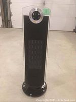 Front view of a black and silver rotating tower heater with circular control panel and vent slots.