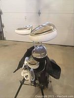 Photo showing multiple Powerbuilt left handed golf clubs standing inside a golf bag on stand in a garage.
