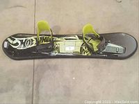 Top view of Hot Wheels branded black kids snowboard with yellow bindings, displaying graphics and model number '7'.