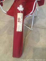 Close-up of the red carrying bag featuring a white maple leaf design, showing some wear and the product label.