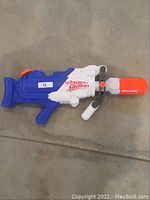 Blue and white Nerf Super Soaker water gun with orange accents shown on concrete floor.