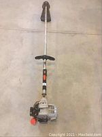 Full view of Echo line trimmer unit lying on floor, showing engine, shaft, and remaining handle grip area missing pull cord and main handle.