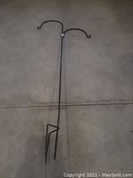 Full length view of the metal shepherds hook lying on the ground showing the entire item with two hooks and pointed end for ground insertion.