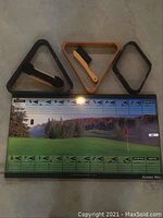 Top down photo of golf-themed billiard game showing scoring board and three different shaped pool racks with two brushes.