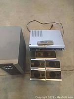 Full view of Toshiba surround sound system main unit with remote control and all speakers including subwoofer and four satellites.