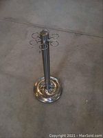 Full view of the stainless steel pool cue stand showing its cylindrical central column, circular weighted base, and 6 round cue holders spaced evenly at the top.