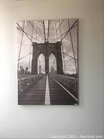 Frontal photo of the black and white bridge canvas art print mounted on wall, showing full view and details of the bridge and cables.