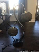 Full view of the retro double globe lamp on a hardwood floor with visible cord, showing stone textured shades on curved metal arms mounted on a round base.