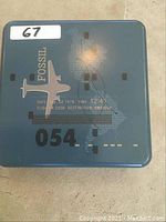 Original metal case packaging of Fossil wallet with aviation graphics and branding.