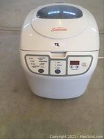 Front-facing view of Sunbeam bread maker showing control panel and lid with viewing window.